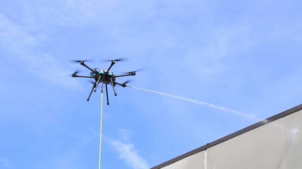Drone power washing service cleaning building surfaces with high-pressure water for maintenance and inspection.